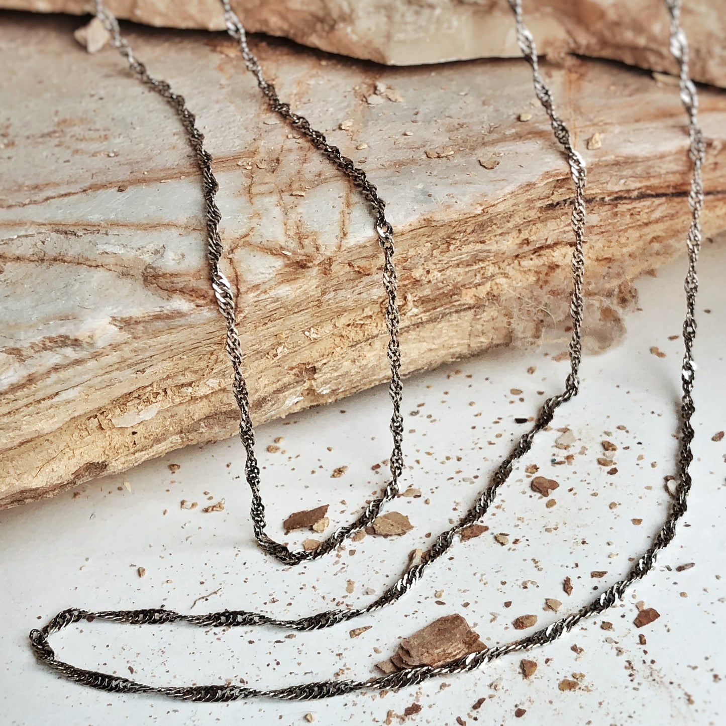 Oxidized sterling silver Singapore chain displayed on light wood with natural texture