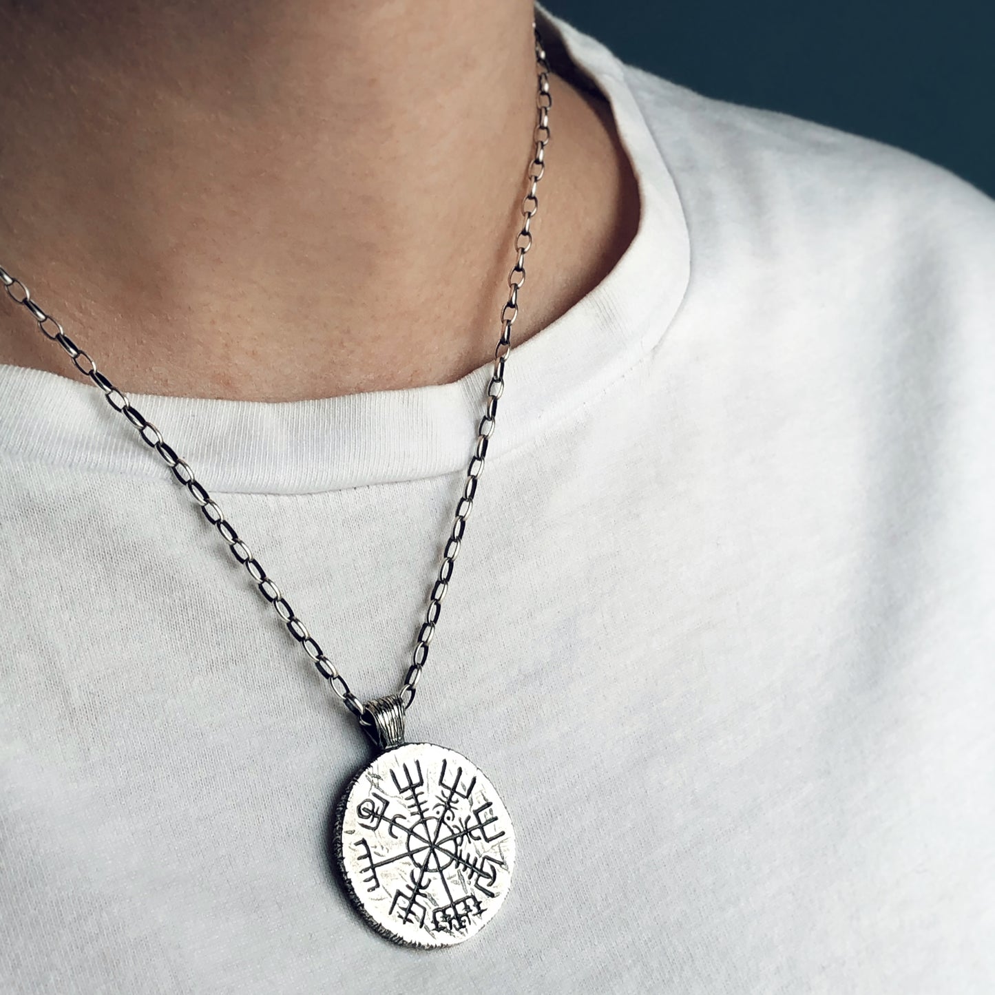 Sterling silver Vegvísir pendant necklace worn on the chest, shown against a white t-shirt. Hand-carved Icelandic symbol, artisan jewelry with mystical and nordic aesthetic.