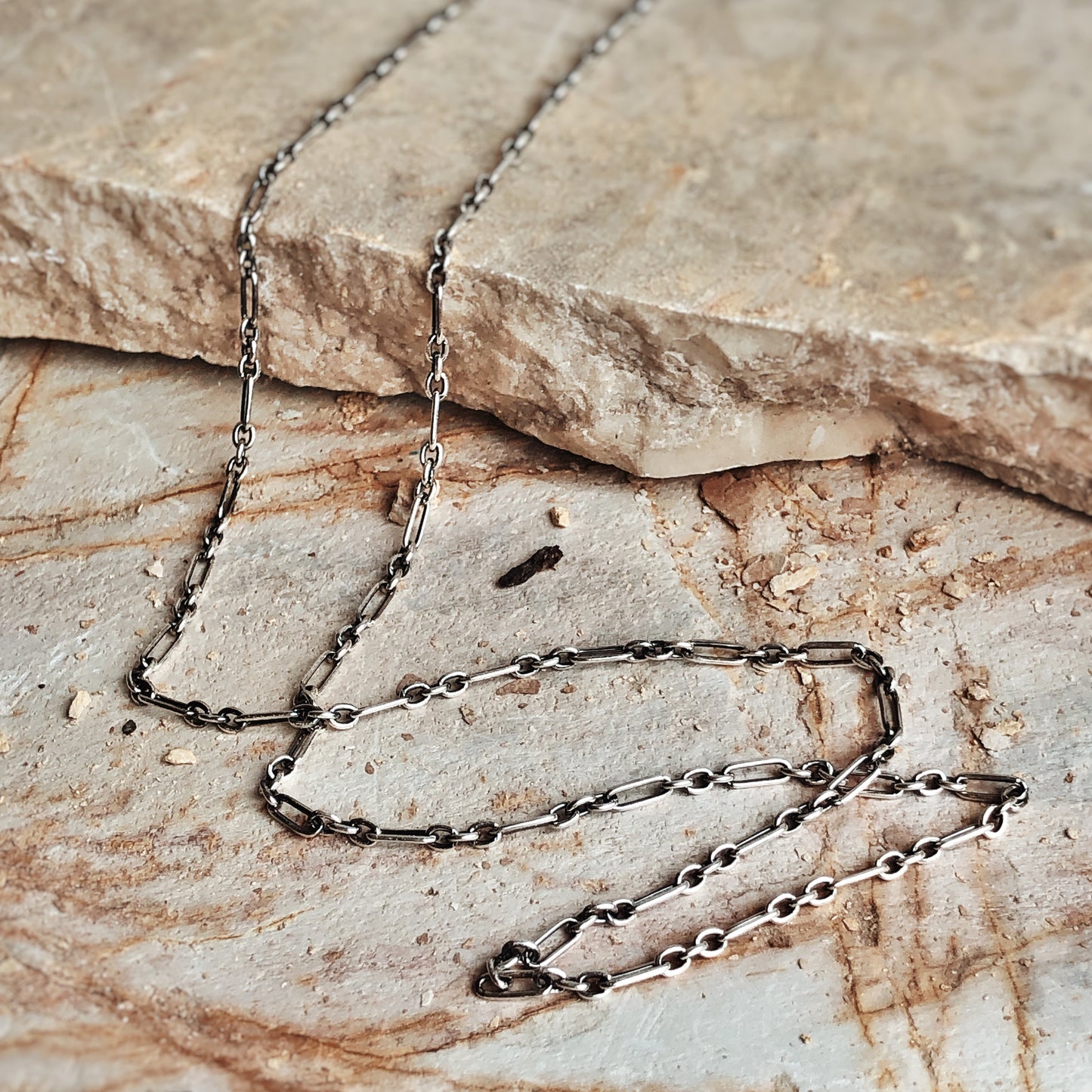 Oxidized silver bar and link chain displayed on a stone surface. Minimalist sterling silver chain for talismans or layering.