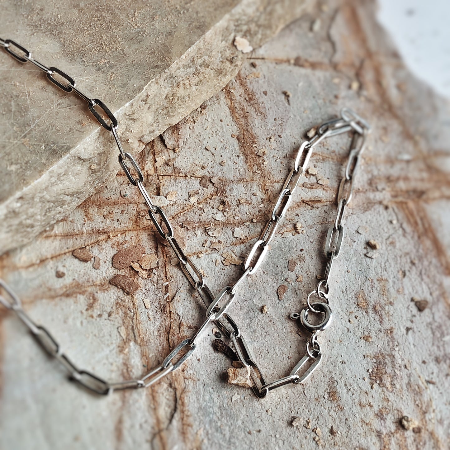 Thick paperclip chain in oxidized sterling silver, shown coiled on textured stone surface with visible clasp. Chunky silver chain necklace for pendants or standalone wear.