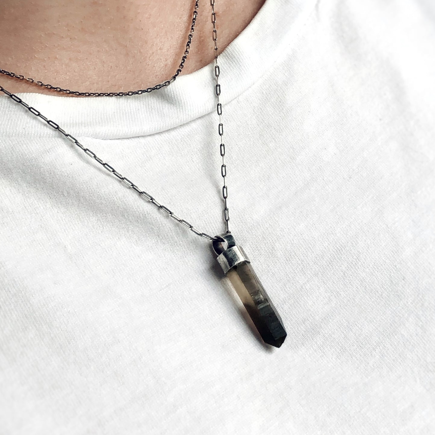 moky quartz pendant with raw point set in oxidized silver, worn on a layered chain over a white shirt