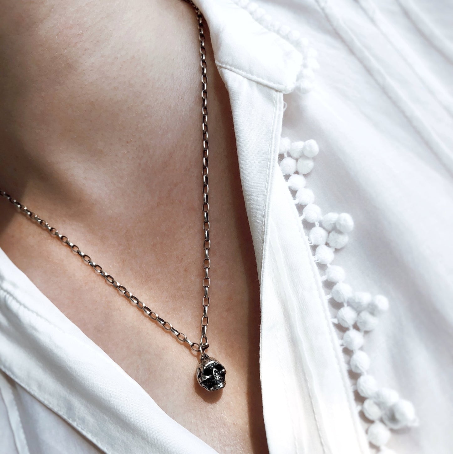 Sterling silver rolo chain necklace with oxidized finish, worn with skull pendant over white shirt
