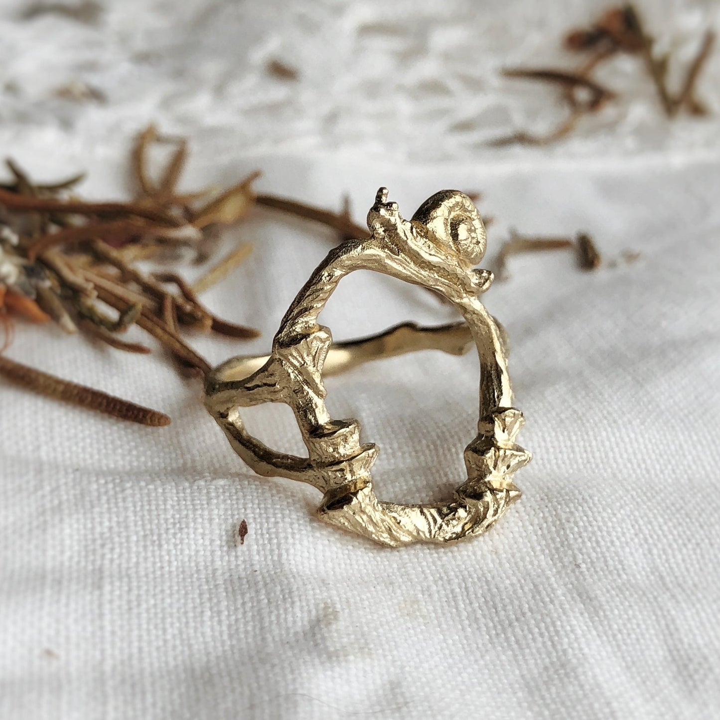 Sculptural 9K gold ring with snail and mushrooms on white fabric with botanical background
