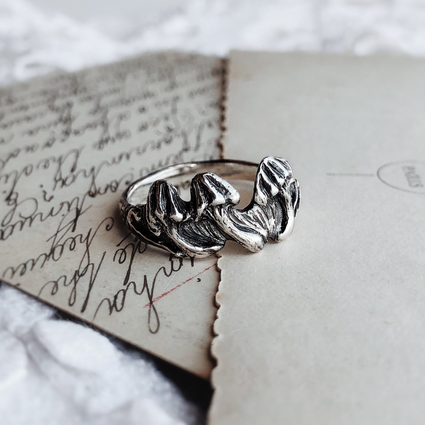 Sculpted sterling silver ring shaped like clustered mushrooms, placed on vintage-style paper. Botanical artisan jewelry with oxidized finish, fairycore and cottagecore inspired.