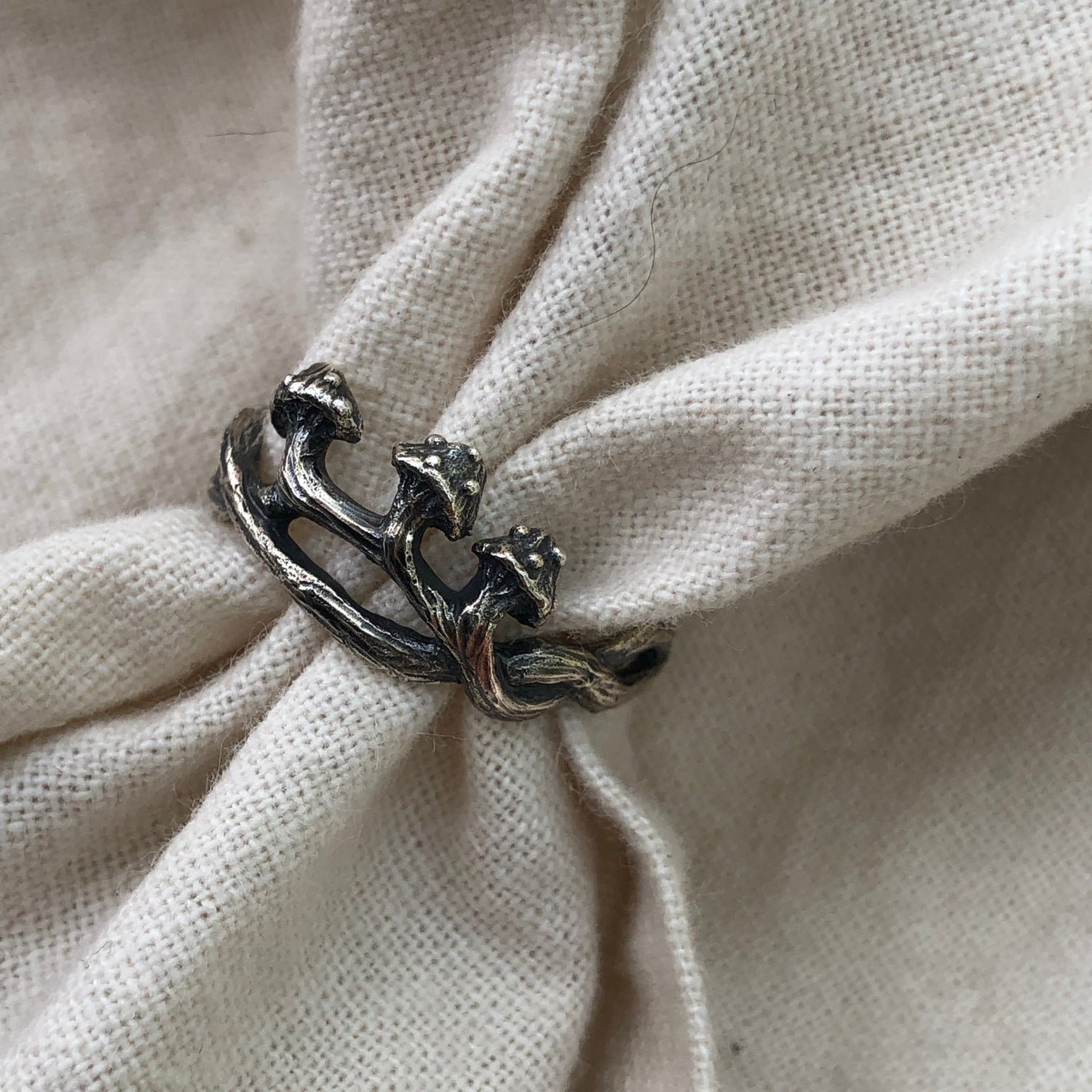 Sterling silver mushroom ring resting on soft beige fabric, showcasing sculpted forest-inspired design. Botanical jewelry, cottagecore style, artisan made.